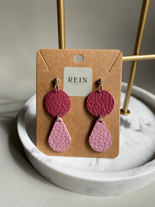 Pair of leather earrings which have a dark pink circle with a light pink teardrop suspended below, on a REIN branded card against a neutral background
