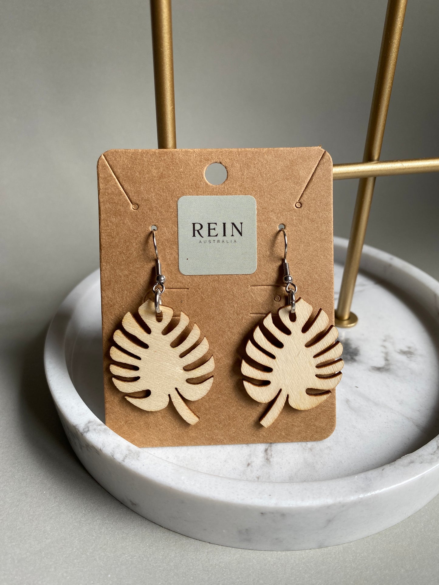 Pair of wooden monsteria leaf-shaped earrings on a REIN branded card against a marble background