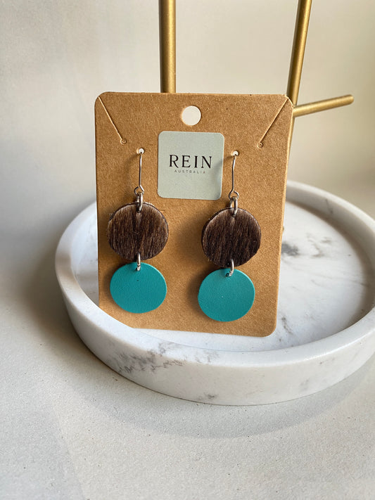 Pair of leather earrings - Dark brown hair-on hide circle with an aqua circle suspended below, with a silver hook against a marble, grey and gold background with REIN branding