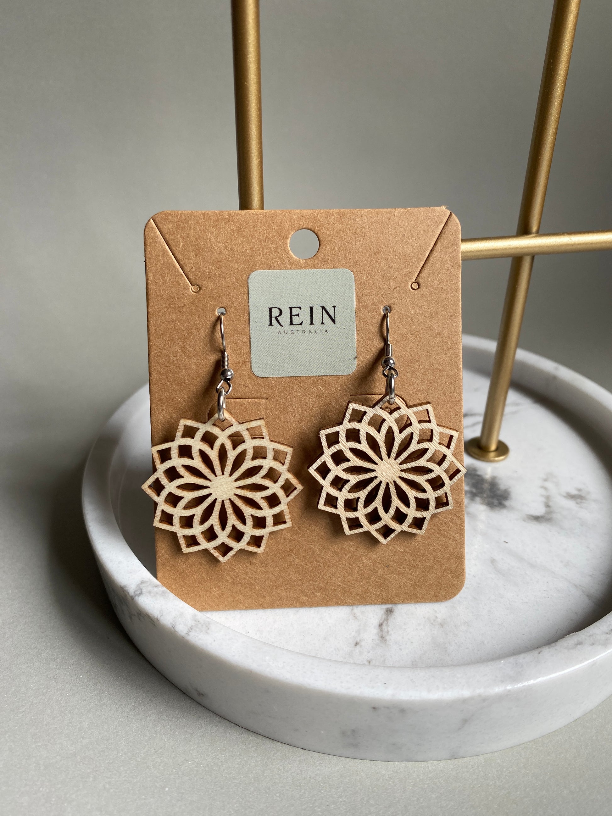 Pair of wooden floral earrings (a chrysanthemum viewed from above) on a REIN branded card against a marble background
