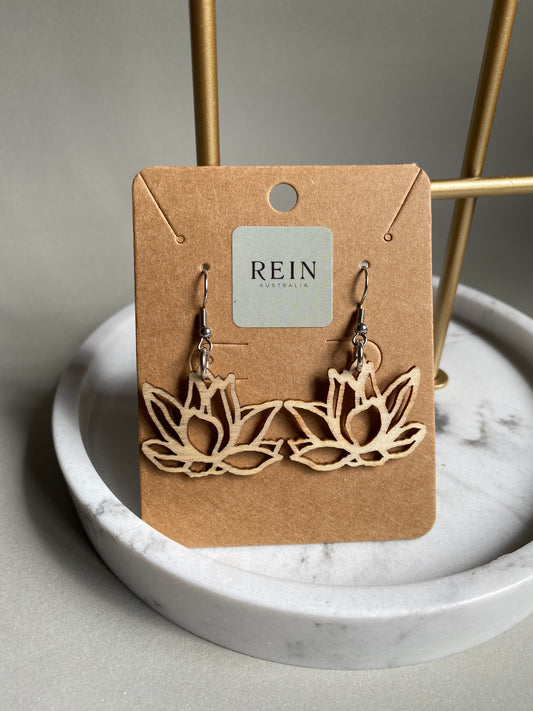 Pair of floral wooden earrings (a lotus flower viewed from side on) a REIN label card against a marble background