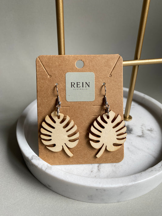 Pair of wooden monsteria leaf-shaped earrings on a REIN branded card against a marble background